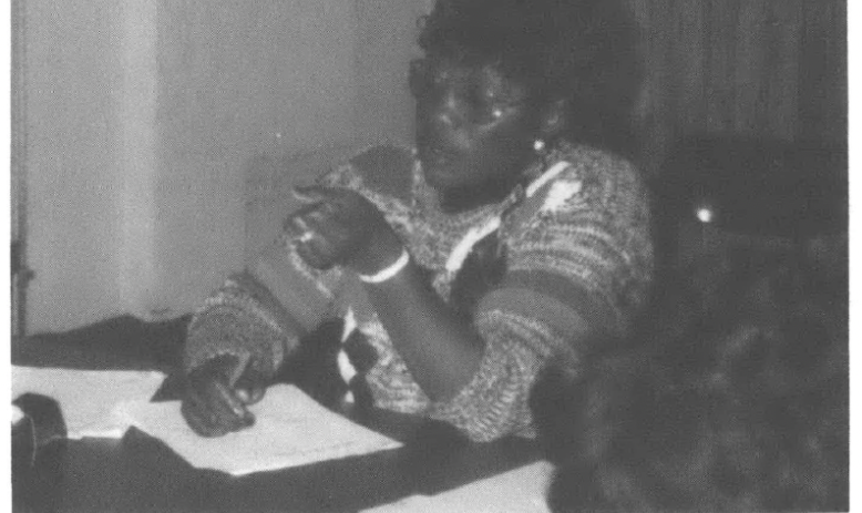 Woman in a sweater at table with a hand holding a pen resting a piece of paper