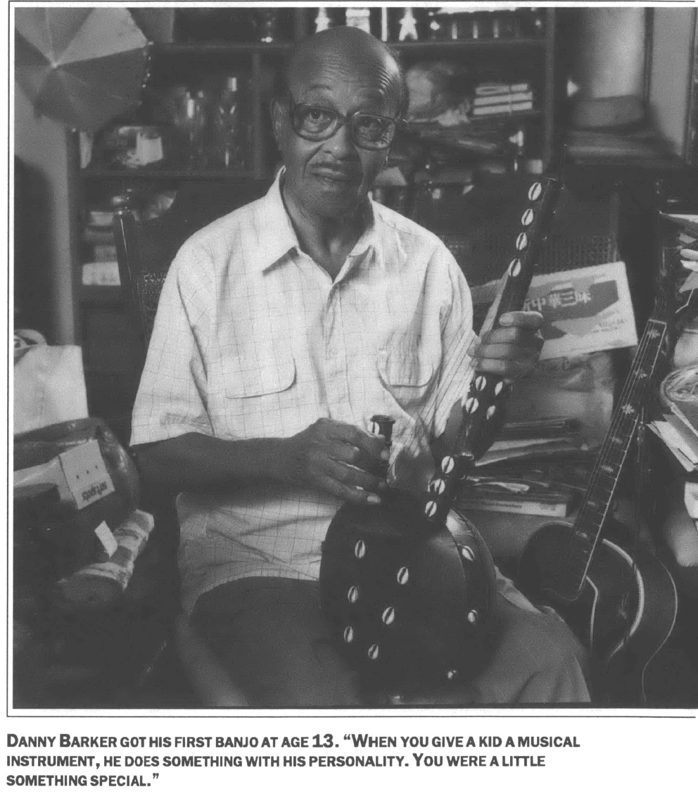 man sitting in ass living room guitar in the background holding an african style harp 