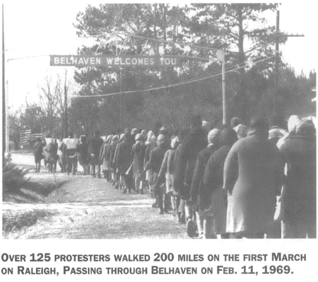 Photo from behind a long column of marchers on a gravel road. Caption reads "Over 125 protestors walked 200 miles on the first March on Raleigh, passing through Belhaven on Feb. 11, 1969."