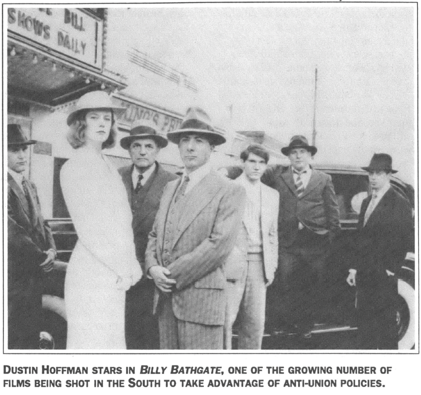 7 people posing seriously in suits and hats standing infront of cars and theater
