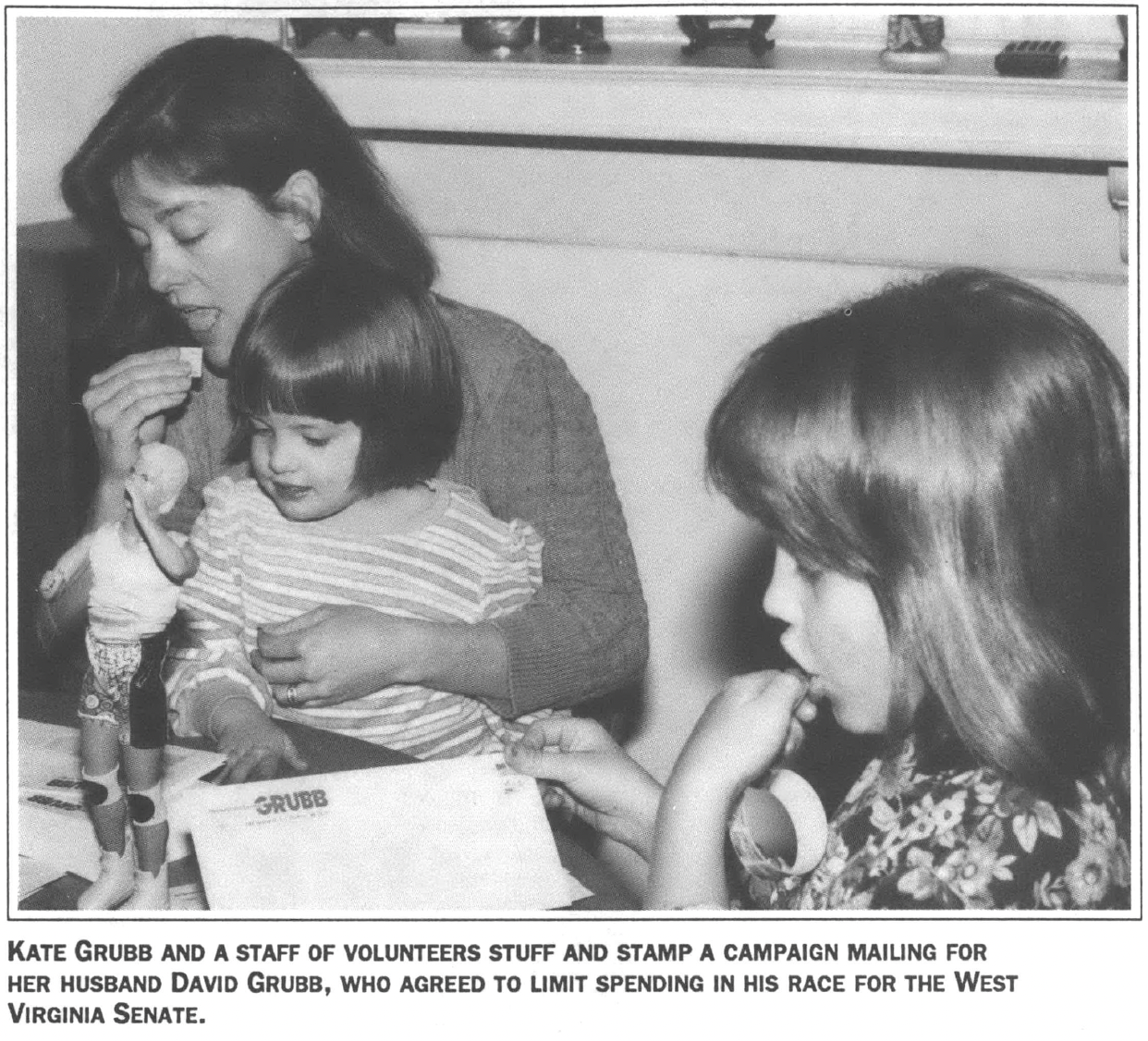 Woman seated holding one child, another sits next to her reading