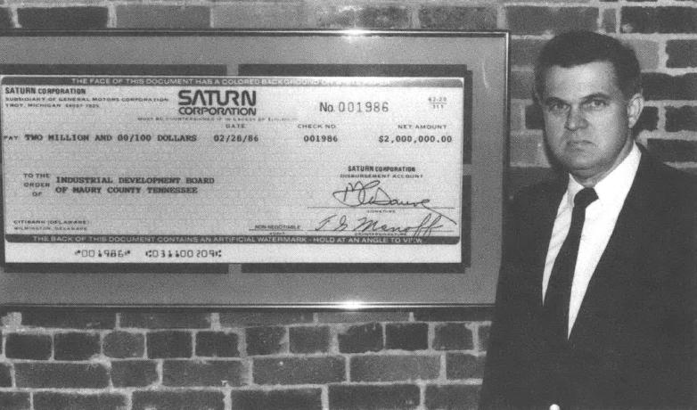 Photo of white man in suit standing next to a large check