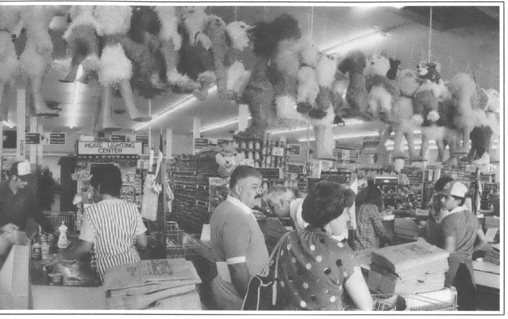 black and white lasndscappe photo of three check out aisles at a grocery store, with people checking out and a line of piñatas hanging over head from a line