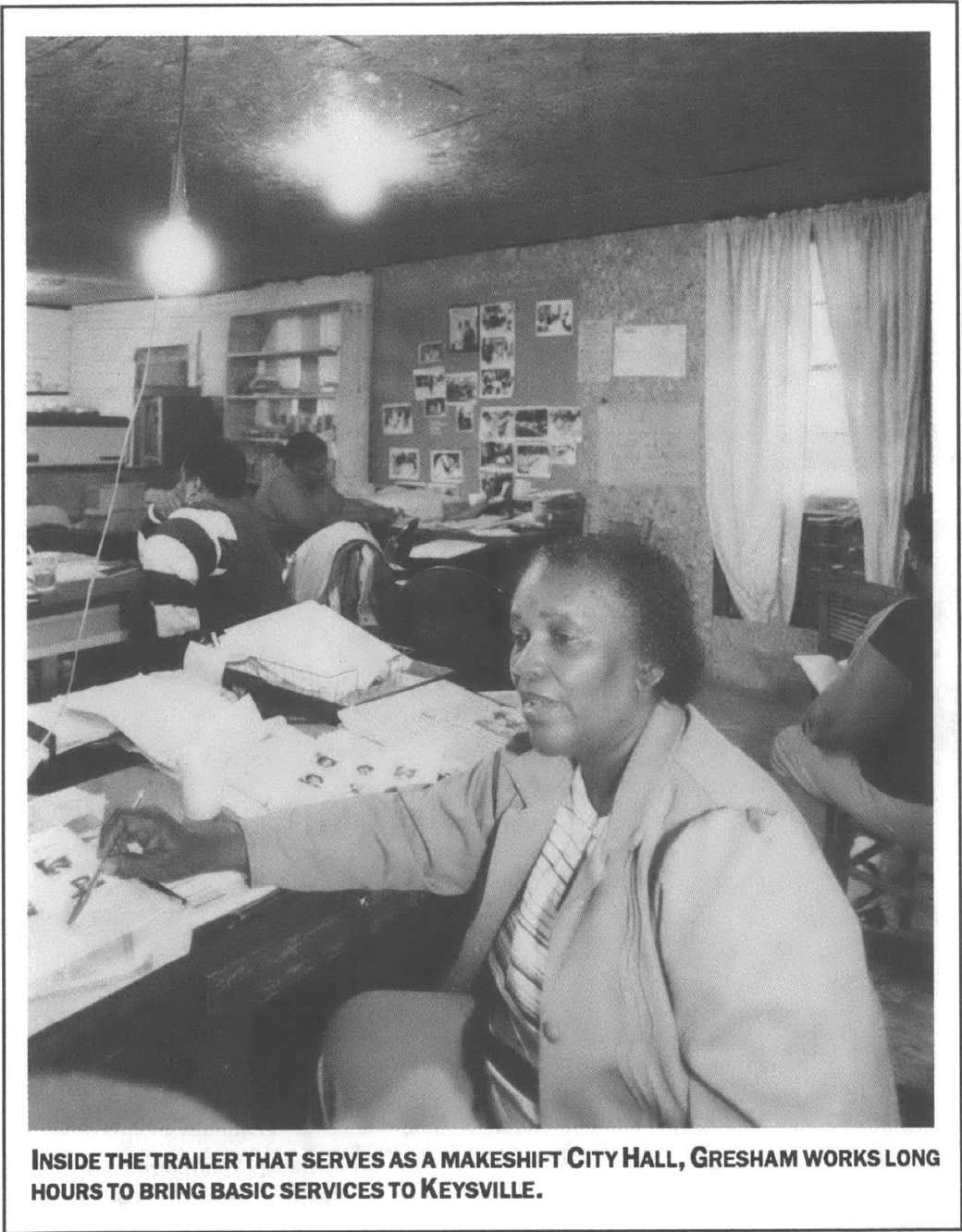 woman sitting at a desk pointing to a page with her pen, 4 others sitting at desks behind her in a trailer black and white photo