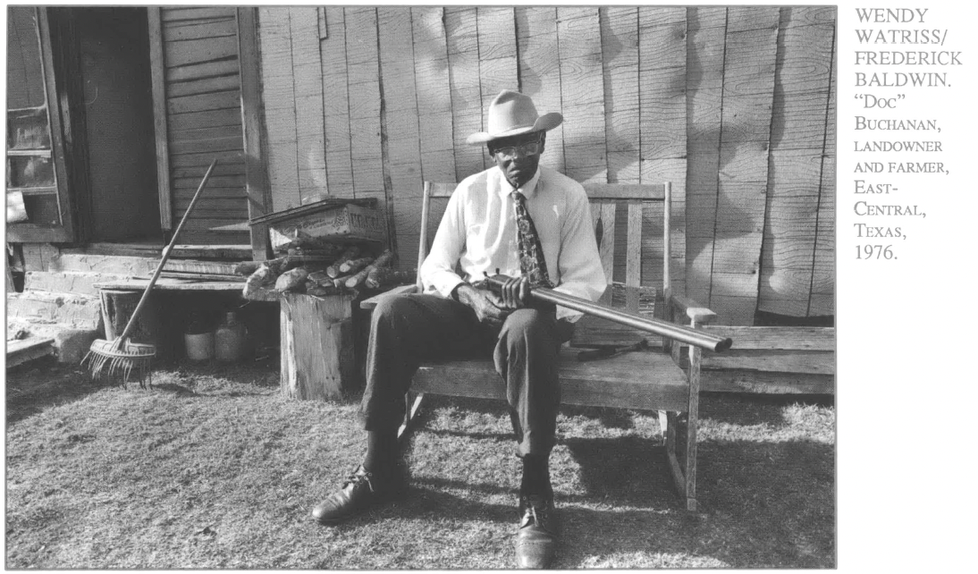 Black man in cowboy hat sitting on bench outside holding a rifle