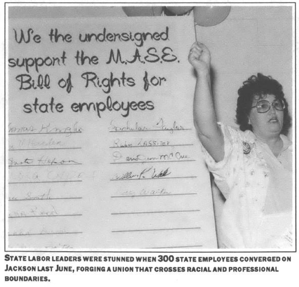 woman stands with her fist raised in front of a large board that reads "We the undersigned support the M.A.S.E. Bill of Rights for state employees" 