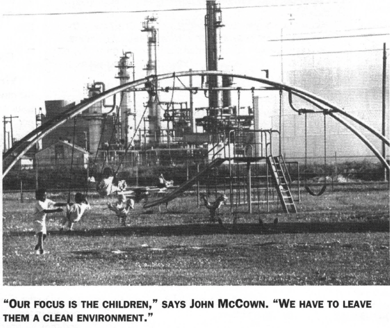 Black and white photo of children playing on a playground in front of an industrial facility