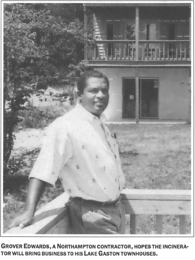 man standing on a porch leaning on railing in a white shirt backyard in a background