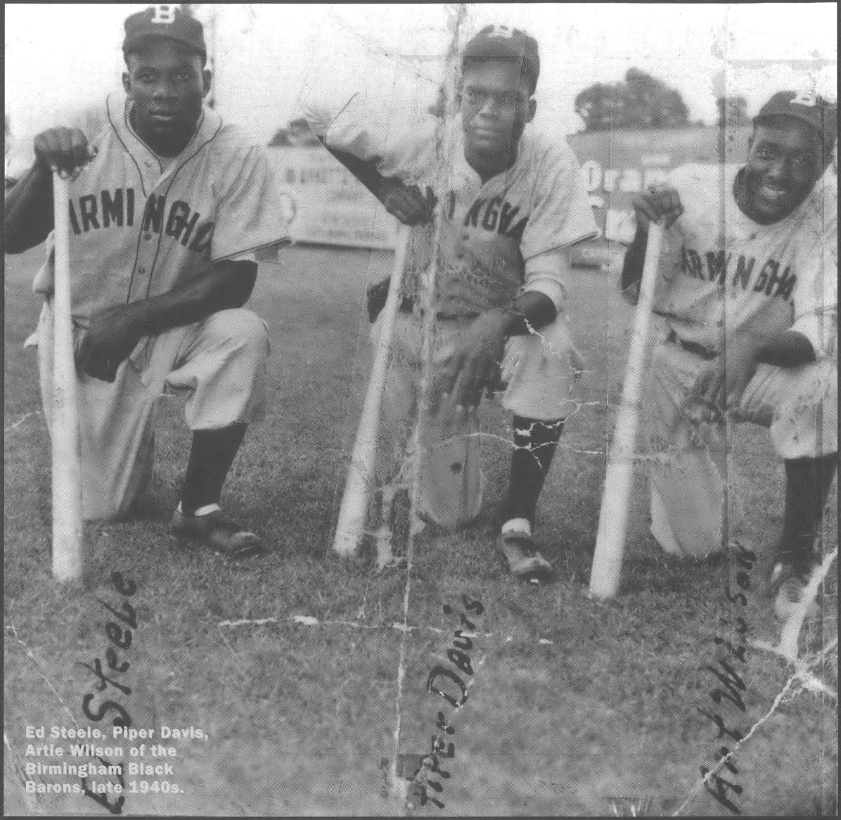 Old photo of three Black baseball players in uniform kneeling with bats