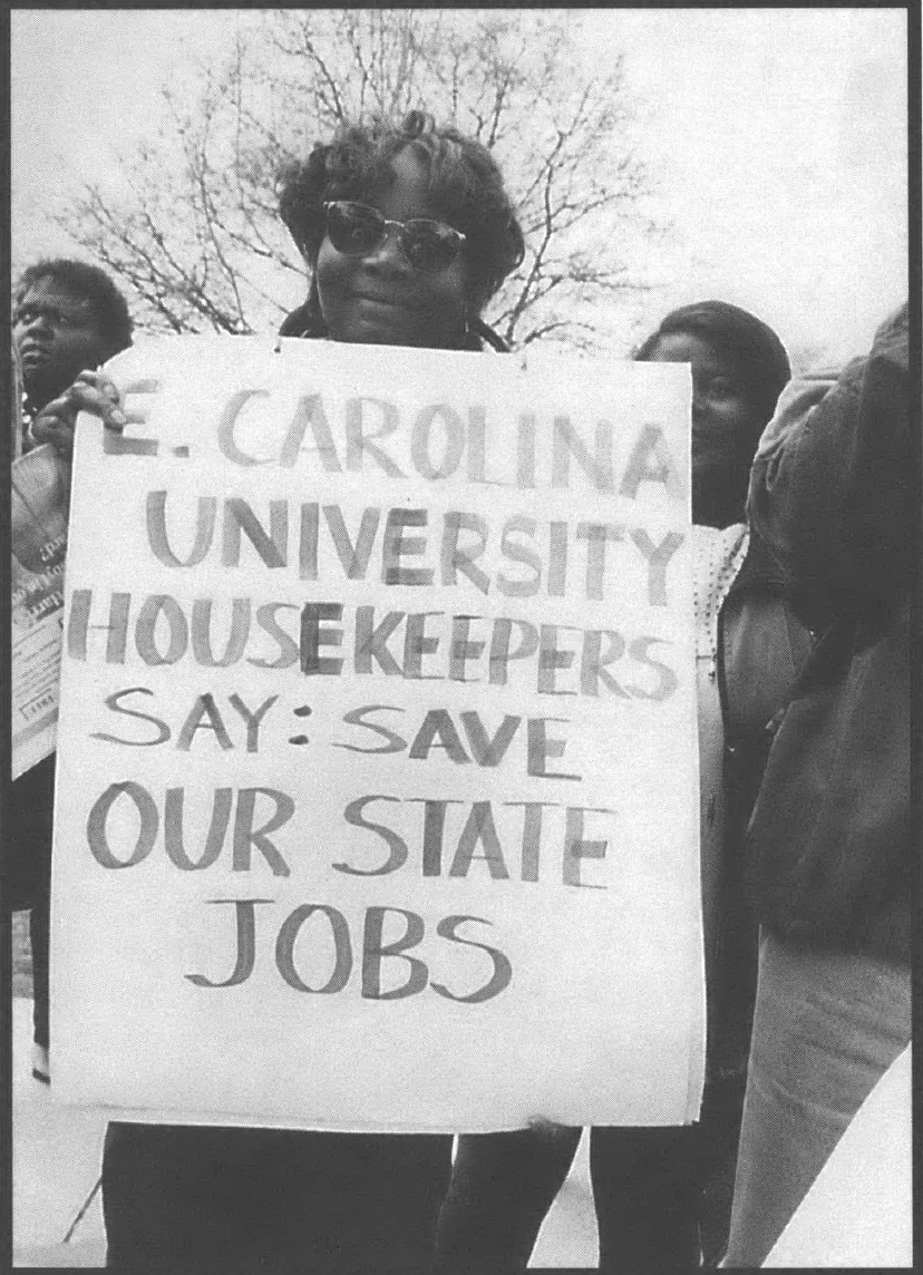 Woman holding sign that says "E Carolina Universty Housekeepers Say: Save Our State Jobs"