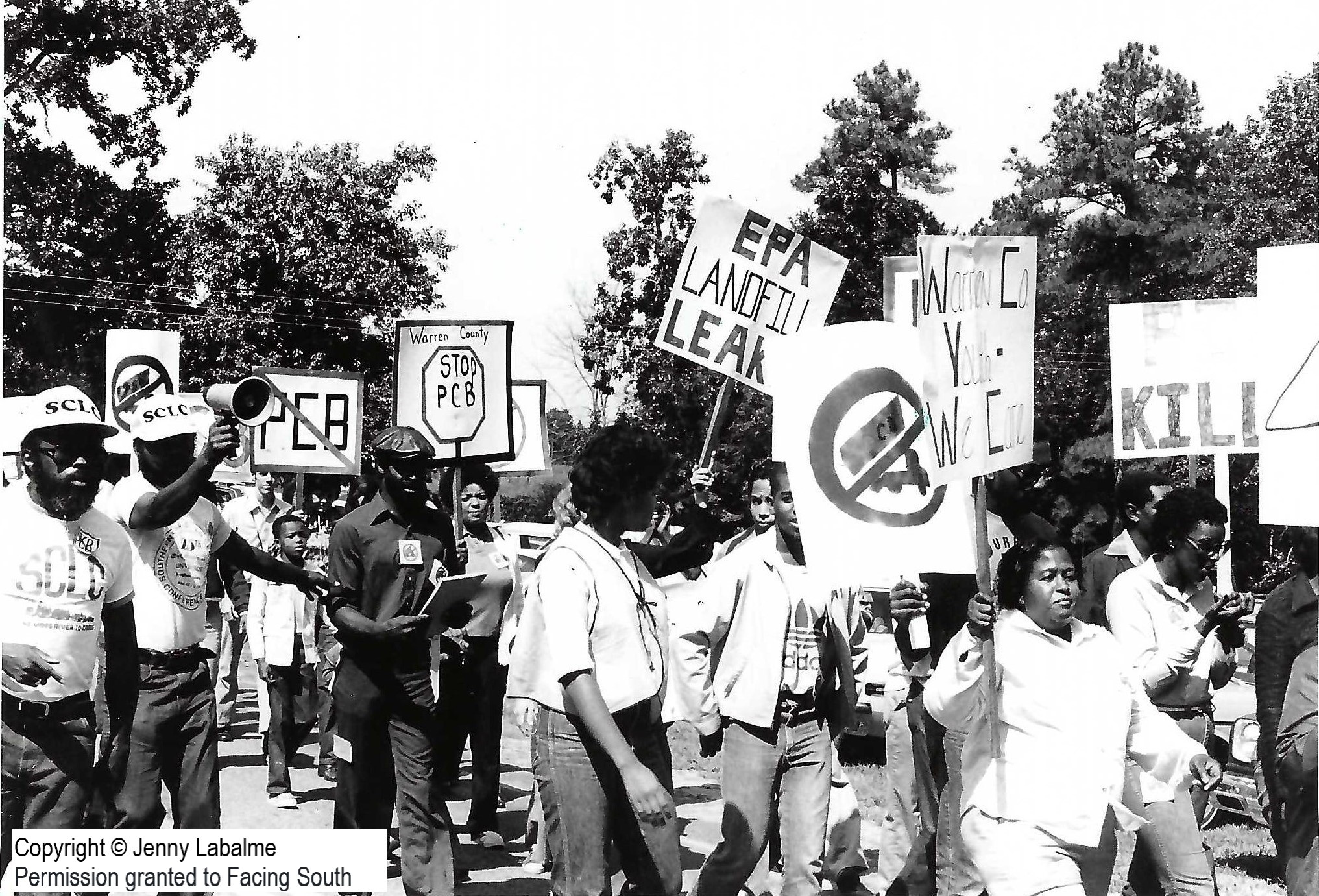 Several demonstrators, some wearing caps that read SCLC, walking and holding signs that say Stop PCB, EPA Landfill Leaks, and other slogans