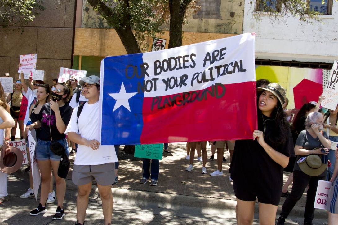 A man and a woman hold a Texas flag with the text "Our Bodies Are Not Your Political Playground" written on it